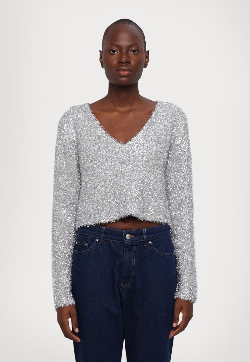 Sølv, fluffy strikket kort genser med V-hals og lange ermer, kombinert med mørkeblå denimjeans med knapp og lommer.