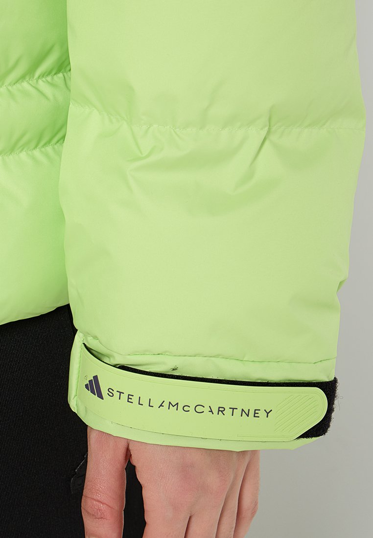 Manica di giacca puffer verde neon con una fascia in velcro. Presenta il logo Adidas e la scritta "STELLA McCARTNEY" stampata in nero. Texture liscia.