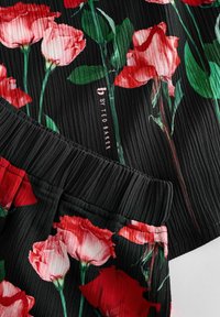 Tessuto nero con stampa floreale di rose rosse e rosa. Texture plissettata con cintura elastica. Etichetta "b by Ted Baker" visibile.