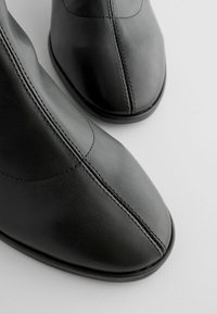 Black leather ankle boots with a pointed toe, featuring visible stitching and a smooth texture. Minimalistic design with a sleek silhouette.