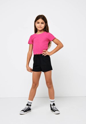 Haut rose à manches courtes à côtes avec un ourlet volé associé à un short noir. Le mannequin porte des baskets montantes noires et des chaussettes blanches rayées.