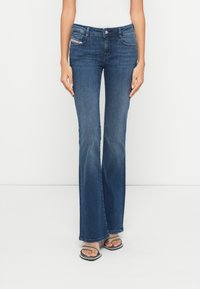 Προσαρμοσμένα τζιν καμπάνα σε σκούρο μπλε χρώμα, με κλασικό σχέδιο πέντε τσεπών, διακοσμητικές ραφές και διακριτική υφή που δείχνει ελαφρώς φθαρμένα.