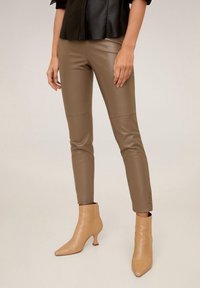 Ruske faux nahkahousut, joissa on istuva muotoilu, sivusaumat ja sileä pinta. yhdistettynä vaaleanbeigeihin nilkkabootseihin.