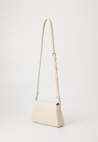 Beige leather crossbody bag with a triangular shape, adjustable strap, silver hardware, and a smooth texture. Minimalist design with no patterns.