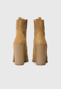 Kamelkleurige enkellaarsjes met een suede afwerking, blokkeren, ribbelstof aan de bovenkant en een trekhaak. Beschikt over een gladde, ronde neus en een stevige zool.