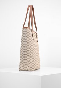 Beige toteväska med bruna läderremmar, med ett mönster av sammankopplade MK-logotyper. Stabil form, slät textur, minimal beslag.