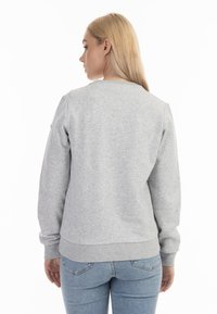 Grijze sweatshirt met een ronde halslijn en geribde manchetten, met een gladde textuur en een strakke pasvorm, gedragen met lichtblauwe jeans.