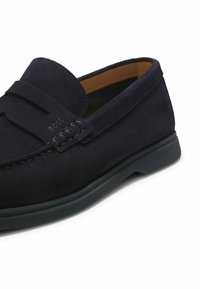 Mocassin en daim bleu marine foncé avec détails cousus, doublure intérieure douce et semelle en caoutchouc noir texturée.