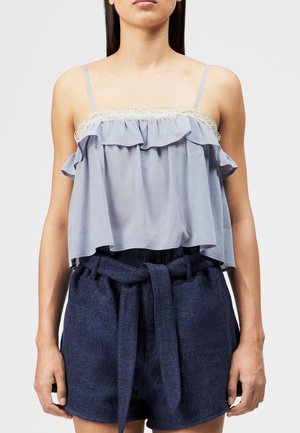 Ung kvinne iført en lyseblå rysjekami med blonder og marineblå høytlivsshorts med knytt stoffbelte.