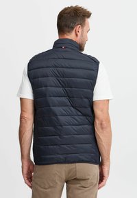 Navy padded vest with a high collar, horizontal stitching, and a small logo accent. Designed for warmth and casual wear.