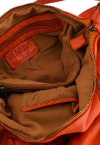 Pomarańczowa skórzana torebka od wewnątrz ma brązowe materiałowe wykończenie. Posiada główną komorę oraz kieszeń na zamek. Metka głosi "VENEZIA Genuine Leather."