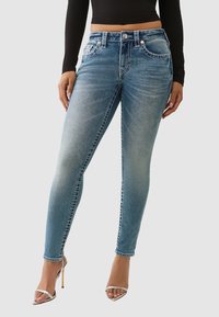 Jean skinny bleu clair avec un effet délavé, doté de poches avant, de détails de couture et d'un ourlet légèrement raccourci. Associé à des talons argentés.