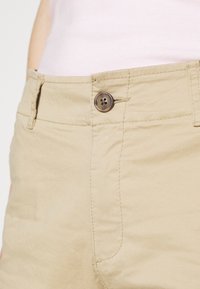 Shorts en coton beige avec fermeture à boutons sur le devant, détails de couture subtils et une texture lisse. Convient pour une tenue décontractée.