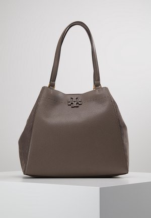 Sac à main en cuir taupe avec finition texturée, forme structurée, double poignée et petit fermoir métallique à l’avant, présenté sur un socle blanc.