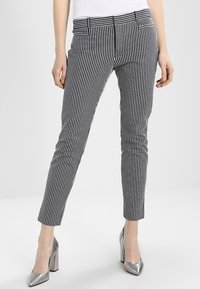 Pantaloni a righe bianche e nere con design aderente, lunghezza alla caviglia e tasche frontali. Indossati con scarpe con tacco alto argentate.
