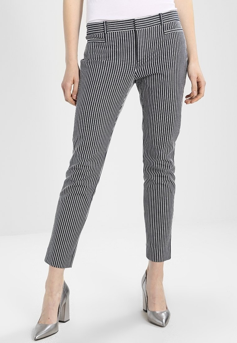 Pantaloni a righe bianche e nere con design aderente, lunghezza alla caviglia e tasche frontali. Indossati con scarpe con tacco alto argentate.