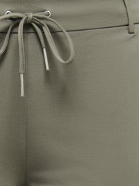 Gros plan sur un pantalon vert olive avec une taille à cordon noué, des embouts métalliques et un détail de couture.