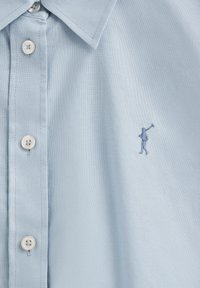 Ljusblå skjorta med knappar, tillverkad av vävt tyg med en jämn struktur och en broderad figur-logga på vänster bröst.