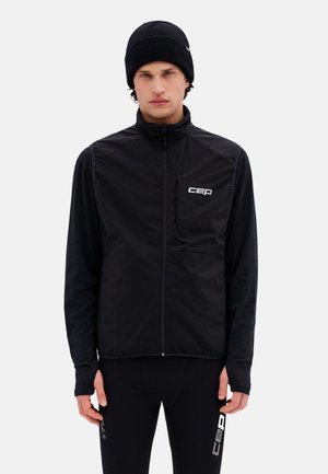 Uomo che indossa un berretto nero, un gilet nero con zip con logo "cep" e leggings sportivi neri con marchio "cep" sulla coscia sinistra.