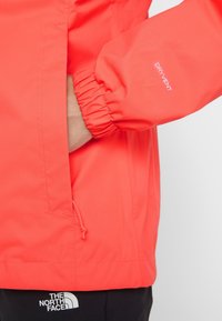 Waterdichte rode jas met elastische manchetten, verstelbare zoom en "DRYVENT"-branding. Voorzien van een handzak met strakke stikseldetails.