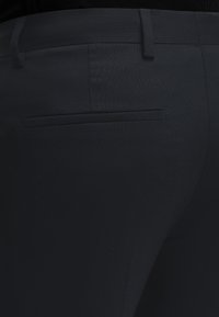 Primo piano di pantaloni neri su misura che mostrano una tasca posteriore a filetto e passanti per cintura su tessuto liscio.