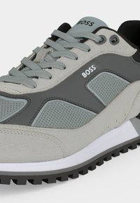 Gros plan d'une basket BOSS grise et bleu clair avec des panneaux texturés, des lacets gris et une semelle extérieure noire crantée.