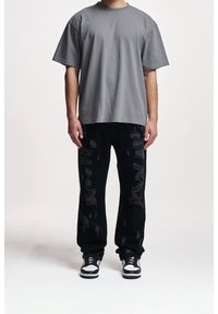 T-shirt gris surdimensionné avec un col rond, associé à un jean noir déchiré avec des détails effilochés et des baskets noir et blanc.