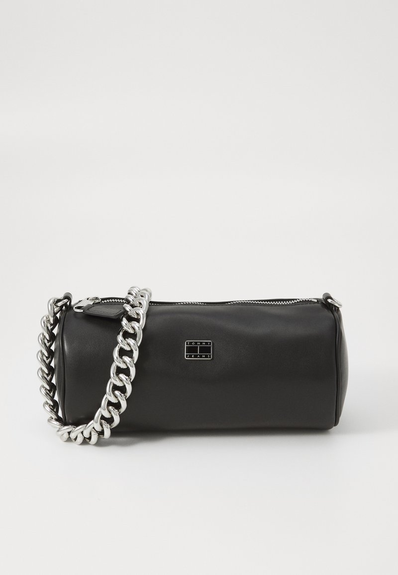 Melna cilindriskā somiņa, izgatavota no gludas ādas. Aprīkota ar sudraba ķēdes siksnu un metāla logotipa plāksni. Ar rāvējslēdzēju augšpusē.