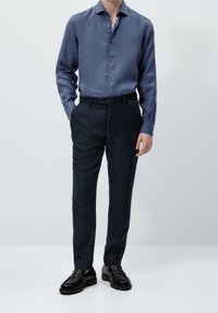 Camicia azzurro chiaro a maniche lunghe con bottoni, abbinata a pantaloni scuri dalla texture particolare. Mocassini neri lucidi completano l'outfit. Design semplice e sartoriale.
