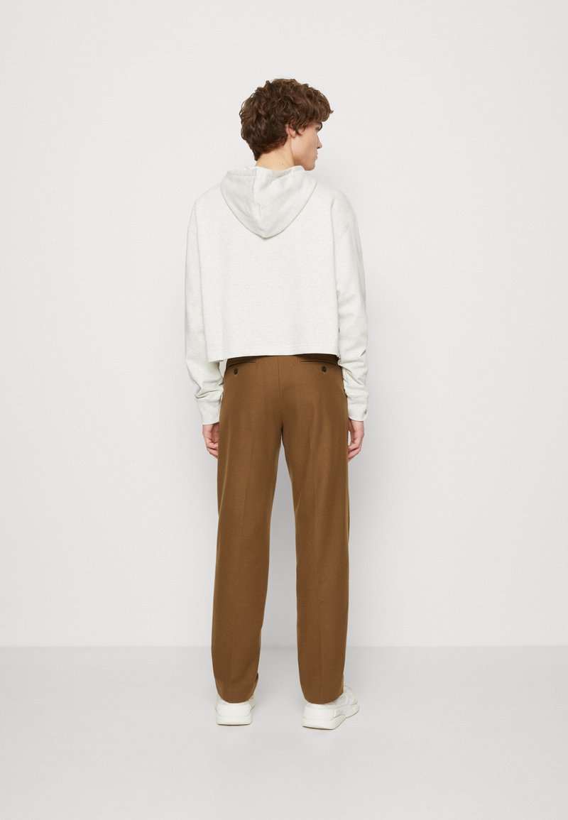 Sweat à capuche gris clair coupé, associé à un pantalon droit marron. La tenue est complétée par des baskets blanches.