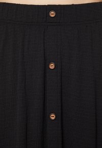 Musta tekstuuriga seelik, millel on kogutud vöökoht ja viis puidust nuppu ees. Kanga välimus on kortsus.