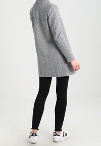 Grijze wollen mix jas met een lange, rechte snit, gecombineerd met zwarte skinny jeans en witte sneakers met zwarte strepen.
