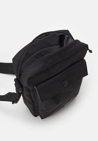 Borsa a tracolla nera realizzata in tessuto testurizzato, dotata di un vano principale con zip, tasca con patta anteriore con chiusura a scatto e tracolla regolabile.