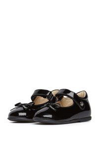 Zapatos Mary Jane de charol negro con punta redonda, acento de lazo y correa ajustable. Acabado suave y interior acolchado.