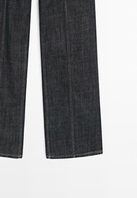 Ciemnoniebieskie dżinsy o prostym kroju, z widocznymi szwami i czystym wykończeniem. Materiał ma gładką teksturę i minimalne detale.