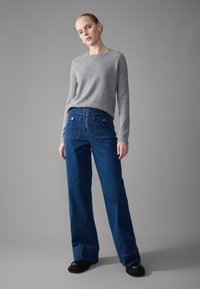 Gray long-sleeve sweater paired with wide-leg blue denim pants featuring a zip front, two back pockets, and contrasting stitching detail. Black shoes.