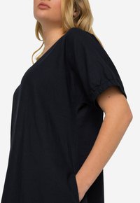 Námořnickomodrá volná šaty s krátkými elastickými rukávy, bočními kapsami a kulatým výstřihem. Měkká, texturovaná látka.