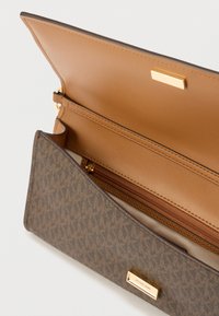 Pruun disainerrahakott monogrammimustriga, avatud klapiga, kuldse kinnitusega ja beeži siseosaga, mis sisaldab lukuga taskut.