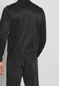 Sort bomberjakke med en glat tekstur, ribbede manchetter og kant, samt en høj krave. Bagsiden viser et minimalistisk design og syninger.