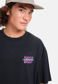 Camiseta de algodón negra con un colorido logo de "Quiksilver" en rosa y verde azulado, de manga corta y cuello redondo.
