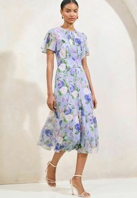 Bloemen midi-jurk van lichtblauwe stof. Korte vlindermouwen, geplooide bovenkant en volle rok. Bevat paarse en roze bloemenpatronen.