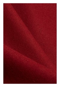 Czerwona wełniana tkanina o miękkiej, teksturowanej powierzchni, wykazująca delikatny połysk i subtelne, bogate zróżnicowanie kolorów w fałdach.