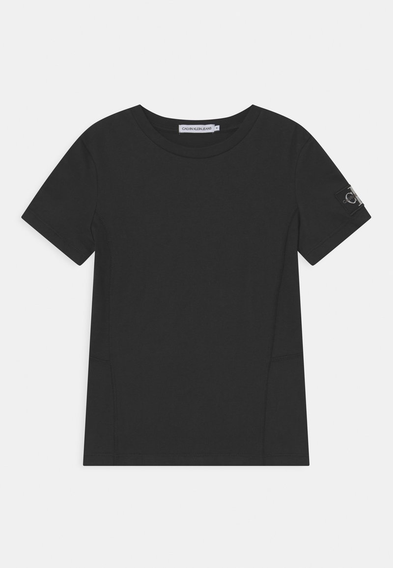 Camiseta negra de manga corta hecha de tejido suave, con cuello redondo, costuras laterales y un pequeño parche de logo en la manga izquierda.