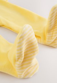 Leotardos amarillos para bebé con rayas horizontales blancas en los pies, extendidos en una superficie clara.