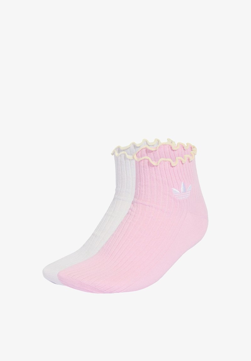 Deux chaussettes basses côtelées avec des bords volantés, une rose avec un logo blanc et une blanche, présentées côte à côte sur un fond blanc.