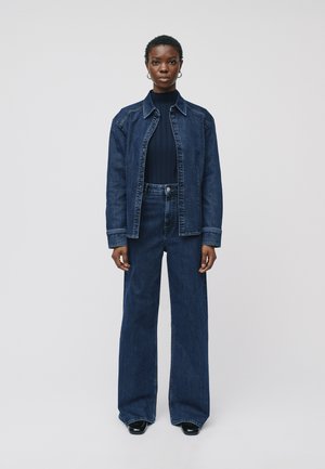 Denimjasje met knopen aan de voorkant en contrasterende stiksels, gecombineerd met hoge taille, brede jeans in een donkere wassing; solide zwart top eronder.