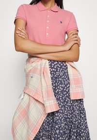 Pink polo shirt with short sleeves and buttons, accompanied by a plaid lightweight shirt draped over a floral-patterned skirt.