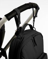 Black backpack hanging from stroller handlebar using adjustable snap-on straps with plastic clips on a white stroller frame.