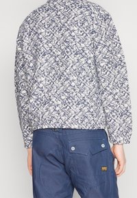 Hvid og marineblå mønstret bomberjakke med elastiske manchetter og kant, kombineret med mørkeblå bukser med baglommer og en logoetiket.