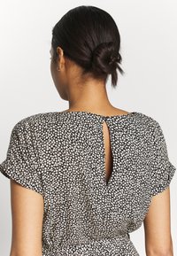 Vestido negro con un patrón floral en color crema. Mangas cortas, detalle en forma de ojal en la espalda con cierre de botón, y cintura fruncida para dar forma.